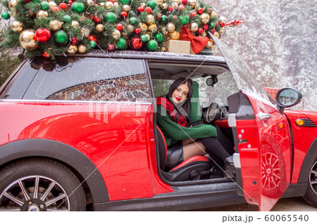 Pretty young girl is sitting in red car with decorated xmas tree on the roof. xmas concept. 60065540