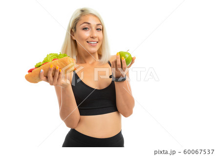 sports girl in a sports uniform shows an apple and fast food on a camera on a white background 60067537