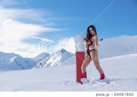 Girl snowboarder in swimsuit stands on the slope with snowboard 60067800