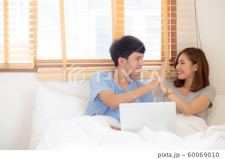 Beautiful young asian couple smiling high five after work laptop on bed in the bedroom 60069010