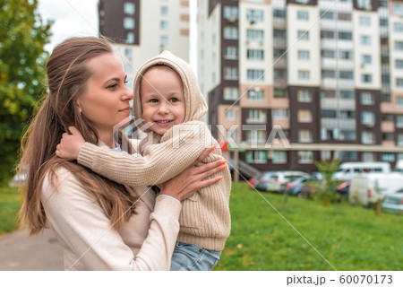 Young happy family, woman mom and little son boy. Hug in autumn on street, smiling for a walk and rejoice. Casual warm clothes with a hood jumper. Free space for copy text. 60070173