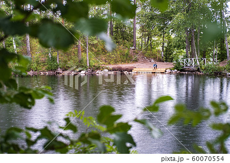 Lonely tourist sits on shore of a beautiful forest lake, in summer rain, in the foreground are 60070554