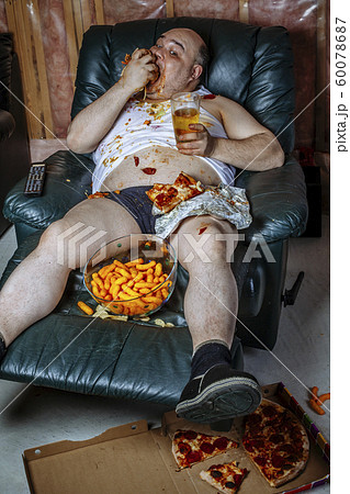 Fat man eating junk food and watching television 60078687