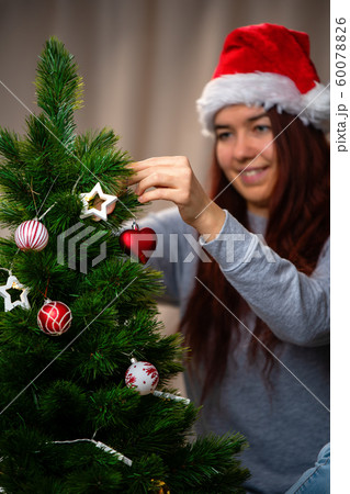 Happy woman in santa hat decorates New Year tree Happy woman in santa hat decorates New Year tree 60078826