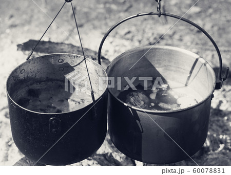 Cooking in two sooty old cauldrons on campfire Cooking in two sooty old cauldrons on campfire 60078831