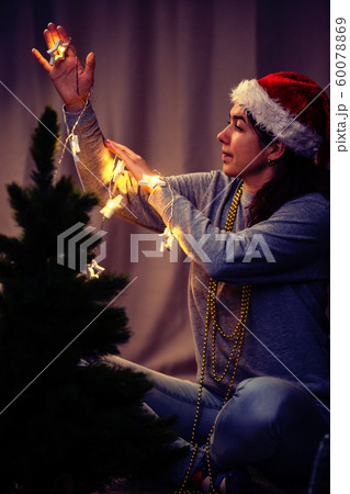 Woman decorates New Year tree with burning garland Woman decorates New Year tree with burning garland 60078869