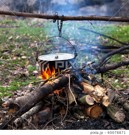 Cooking in old sooty cauldron on campfire 60078871