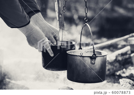 Man cooking in sooty old pots on bonfire Man cooking in sooty old pots on bonfire 60078873