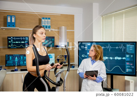 Female athlete testing the stepper with electrodes on her and the doctor follows her 60081022