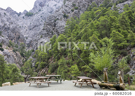 Recreation area with wooden tables and wooden drinking water tank in gorge among mountains and green pine forest. Selective focus. Recreation area with wooden tables and wooden drinking water tank in gorge among mountains and green pine forest. Selective focus. 60082016
