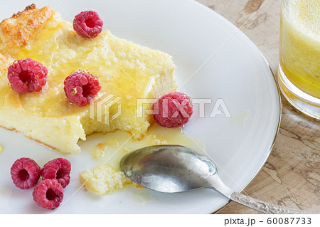 Close-up of curd casserole with raspberries and honey and spoon on white plate and glass with smoothie on wooden saw cut. Cheese casserole recipe contains Close-up of curd casserole with raspberries and honey and spoon on white plate and glass with smoothie on wooden saw cut. Cheese casserole recipe contains 60087733