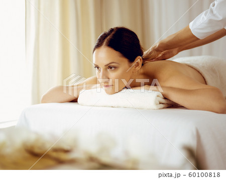 Pretty brunette woman enjoying procedure of back massage in spa salon. Beauty concept Pretty brunette woman enjoying procedure of back massage in spa salon. Beauty concept 60100818