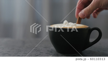 adding cinnamon stick into cappuccino in black cup on terrazzo countertop adding cinnamon stick into cappuccino in black cup on terrazzo countertop 60110313