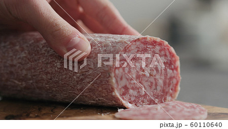 man slicing salame sausage on olive wood board 60110640