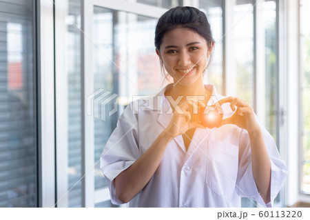 young beautiful doctor woman smile holding red heart with flare light. young beautiful doctor woman smile holding red heart with flare light. 60113220