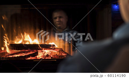 Fire is burning in the fireplace, a man is looking at him. Reflection is visible in the glass Fire is burning in the fireplace, a man is looking at him. Reflection is visible in the glass 60114190