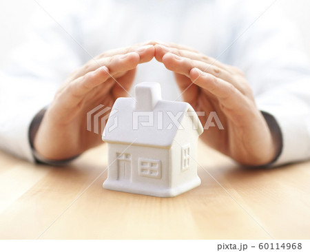 Small white toy house protected by hands 60114968