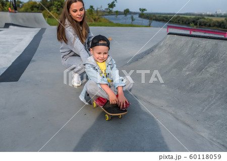 Family mother woman little boy son 3-5 years old, summer sports field in city, playing skateboarding, emotions of joy, fun relaxation on weekend. Everyday clothes, parenting support care for child. 60118059