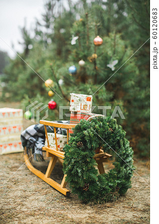 Beatiful wooden Santa's sledge with Christmas gifts and wreath, over the background of winter forest and decorated Christmas tree. Merry Christmas and Happy New Year Concept. 60120683