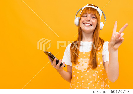 european red-haired girl with red headphones and a phone on a yellow background. 60120713