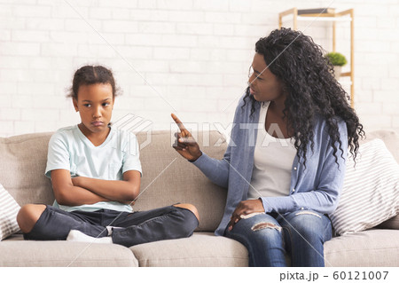 Grumpy black mother scolding her naughty little daughter on sofa at home 60121007