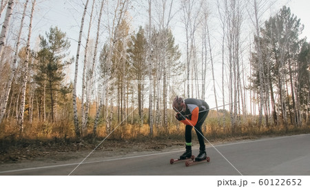 Training an athlete on the roller skaters. Biathlon ride on the roller skis with ski poles, in the helmet. Autumn workout. Roller sport. Training an athlete on the roller skaters. Biathlon ride on the roller skis with ski poles, in the helmet. Autumn workout. Roller sport. 60122652