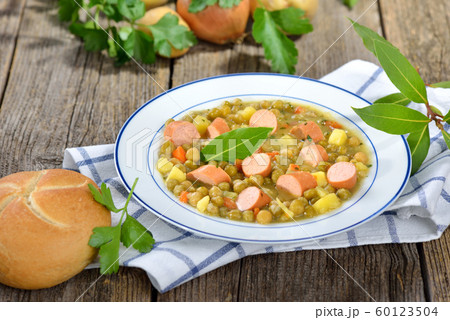 Hearty pea stew with potatoes, bacon and Viennese sausages served in a white plate 60123504