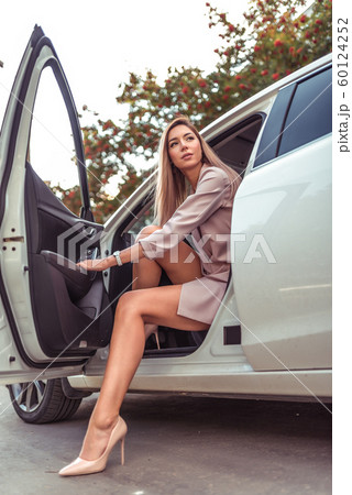 Beautiful girl business lady, in summer in autumn city, gets out of car. A strict suit tanned leather high-heeled shoes. Car rental, car sharing. Car parking, business meeting in city. 60124252