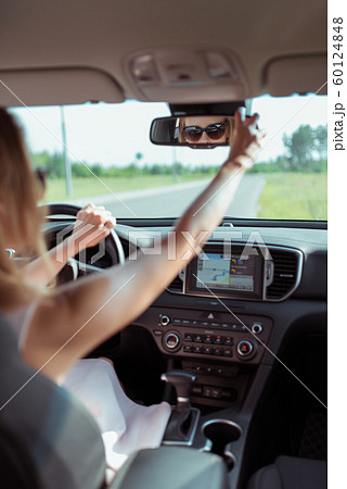 woman looks in rearview mirror, sits in car in summer in city, reversing, checks children and passengers in back seat of car. Sunglasses in summer outside city on highway. 60124848