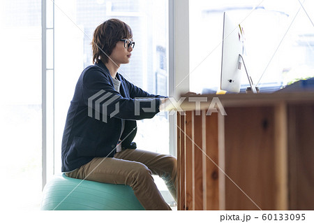 バランスボールに座ってパソコンに向かう若い男性 60133095