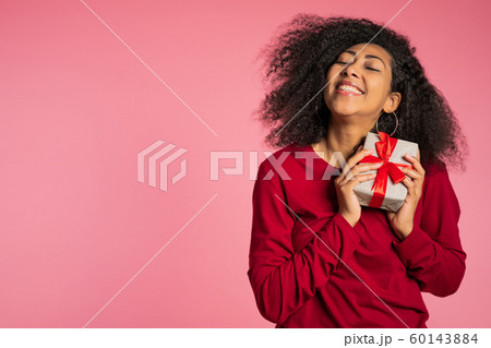Beautiful african american woman received gift box with bow. She is happy and flattered by attention. Girl on studio background. 60143884