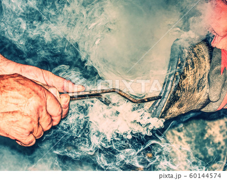 Blacksmith hold horseshoe in long curved pliers on 60144574