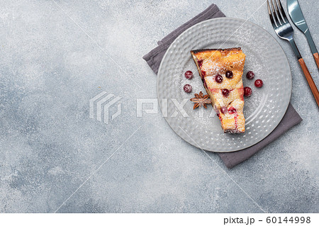 A piece of cottage cheese pie casserole with cranberry berries and spices cinnamon and anise on a plate. Grey concrete background. 60144998
