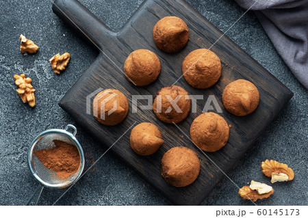 Delicious chocolate truffles sprinkled with cocoa powder and walnuts on a wooden stand. Dark concrete background. Copy space. Delicious chocolate truffles sprinkled with cocoa powder and walnuts on a wooden stand. Dark concrete background. Copy space. 60145173
