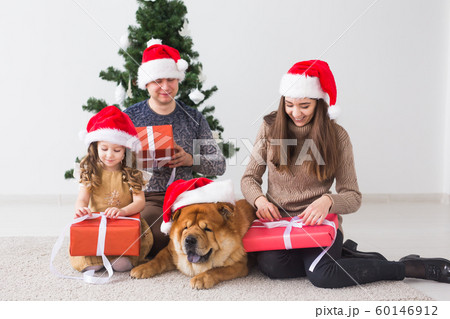 Pet, holidays and festive concept - Family with dog are standing near christmas tree. Pet, holidays and festive concept - Family with dog are standing near christmas tree. 60146912