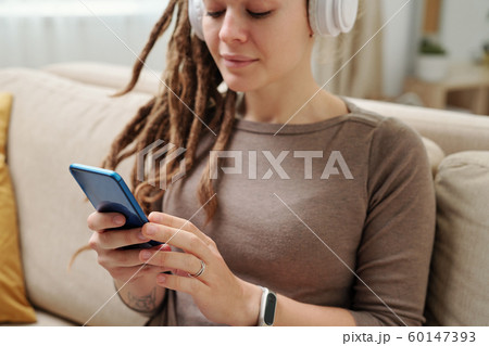 Hands of young woman with headphones scrolling in smartphone for music 60147393