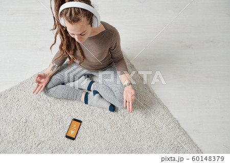 View of serene young woman in headphones sitting in pose of lotus 60148379