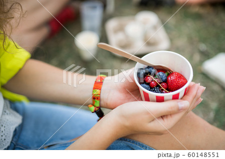 Unrecognizable woman at summer festival, sitting on the ground and eating fruit. 60148551