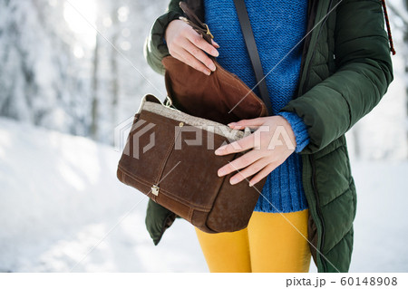 Midsection of woman with handbag standing outdoors in snowy winter forest. 60148908