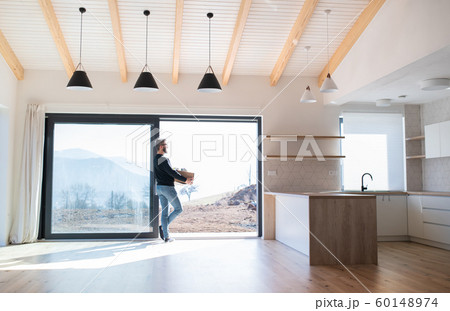 Mature man with moving box standing by patio door in unfurnished house. 60148974