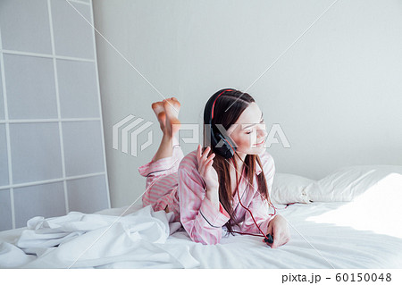 brunette woman in pink Pajamas listening to music with headphones 60150048