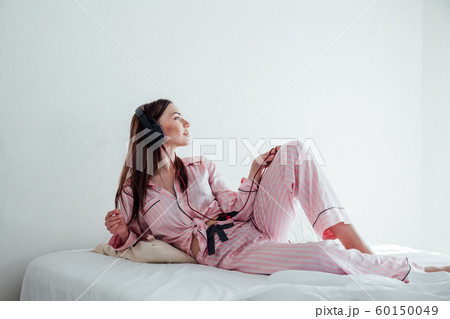 brunette in pink Pajamas listening to music with headphones on the bed brunette in pink Pajamas listening to music with headphones on the bed 60150049