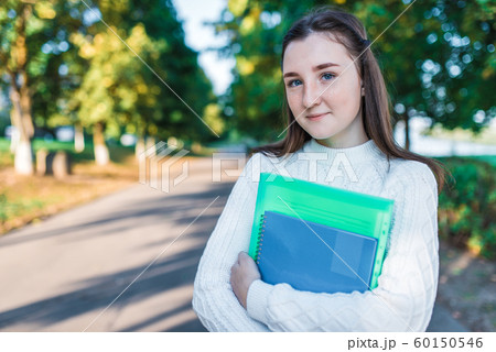 Teenager girl 14 years old autumn day summer city, hands notebooks folders with notes, happy smiling smart student, casual clothes, sweater, outdoors portrait teenager schoolgirl. Free space for text Teenager girl 14 years old autumn day summer city, hands notebooks folders with notes, happy smiling smart student, casual clothes, sweater, outdoors portrait teenager schoolgirl. Free space for text 60150546