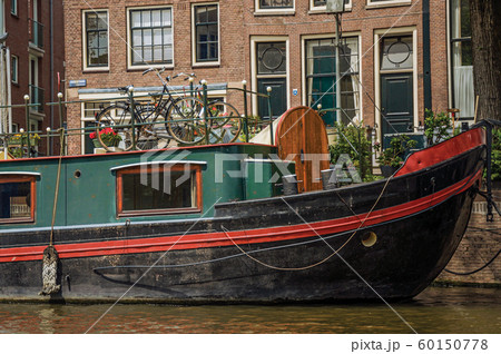Big boats moored at canal side and old buildings in Amsterdam 60150778