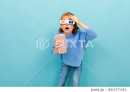 surprised girl in movie glasses is holding popcorn in her hands on a light blue background 60157181