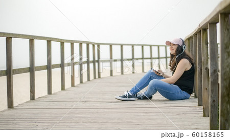 Young woman sits on a wooden pier at the beach 60158165