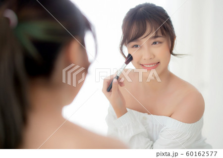Beauty portrait young asian woman smile with face looking mirror applying makeup with brush cheek Beauty portrait young asian woman smile with face looking mirror applying makeup with brush cheek 60162577