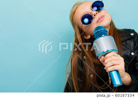 portrait of a smiling european girl in sunglasses singing with a microphone on a light blue wall portrait of a smiling european girl in sunglasses singing with a microphone on a light blue wall 60167334