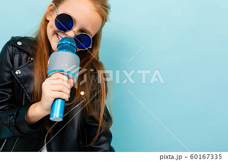 portrait of a smiling european girl in sunglasses singing with a microphone on a light blue portrait of a smiling european girl in sunglasses singing with a microphone on a light blue 60167335