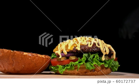 Craft burger is cooking on black background. Consist: sauce, lettuce, tomato, red onion, pickle, cheese, bacon, air bun and marbled meat beef. 60172737